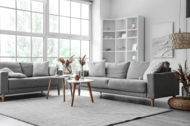 Işıl ışıl oturma odasının içi. Büyük pencerenin yanında rahat gri koltuklar ve kahve masası.