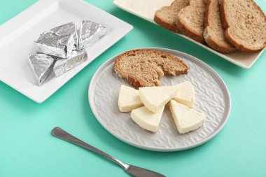 Turkuaz arka planda lezzetli işlenmiş peynir ve ekmek parçaları içeren tabaklar, yakın plan.