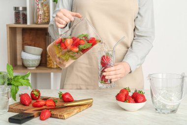 Kadın mutfaktaki sürahide çilekli limonata dolduruyor.