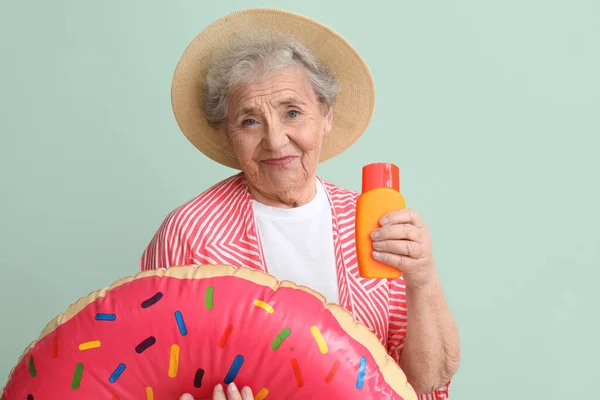 stock image Senior woman with sunscreen cream and inflatable ring on green background