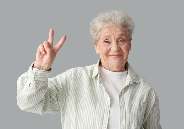 Старшая Женщина Показывает Победный Жест Сером Фоне — стоковое фото