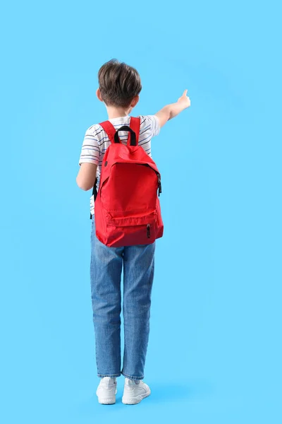 Malý Chlapec Školní Brašnou Ukazuje Něco Modrém Pozadí Pohled Zezadu — Stock fotografie