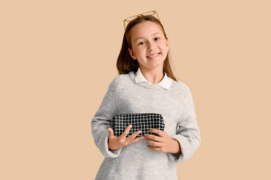 Bej arka planda kalem kutusu olan küçük bir kız.