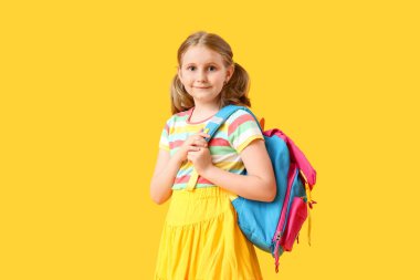 Sarı arka planda sırt çantası olan sevimli küçük bir kız.