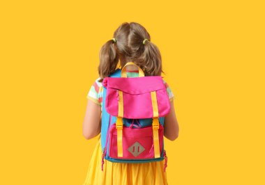 Sarı arka planda sırt çantalı, sevimli küçük bir kız.