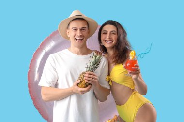Mavi arka planda şişme yüzük, ananas ve kokteyl olan genç bir çift.