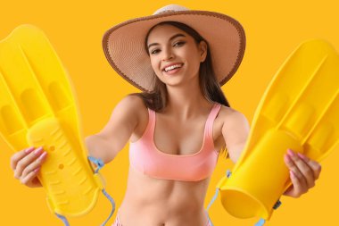 Sarı arka planda paletleri olan yaz şapkalı genç bir kadın.