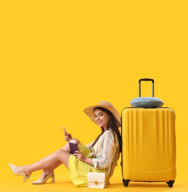 Pasaportlu ve çantalı genç bir kadın sarı arka planda cep telefonu kullanıyor.