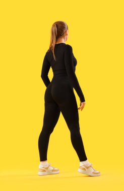 Sarı arka planda spor giyimli genç bir kadın.