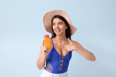 Genç ve güzel bir kadın arka planda güneş kremini işaret ediyor.