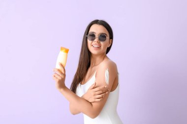 Leylak arka planında güneş kremi olan güzel genç bir kadın.