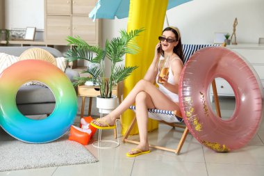 Yaz tatiline hazır genç bir kadın cep telefonuyla evde konuşuyor.