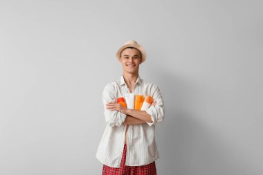 Gri arka planda farklı güneş kremi şişeleri olan mutlu genç bir adam.