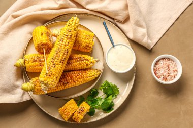 Lezzetli ızgara mısır koçanı ve kahverengi arka planda sos tabağı.