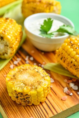 Lezzetli ızgara mısır ve yeşil arka planda sos koçanlarıyla ahşap tahta.