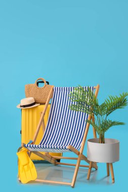 İçinde bavul, plaj aksesuarları ve mavi arka planda palmiye ağacı olan iskemle.