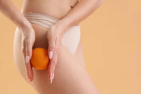 Young woman with cellulite problem and orange on beige background, closeup