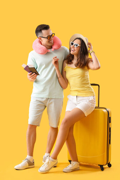 Young couple with passports and suitcase on yellow background