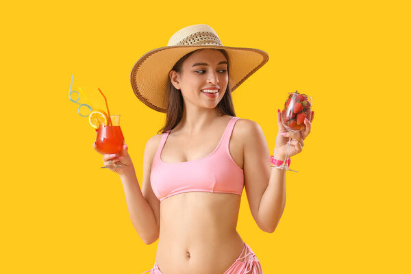 Young woman with summer cocktail and strawberries on yellow background