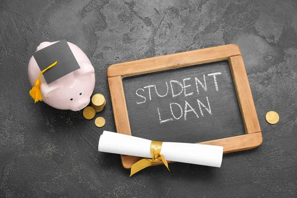 stock image Chalkboard with text STUDENT LOAN, diploma, piggy bank in graduation cap and coins on black background