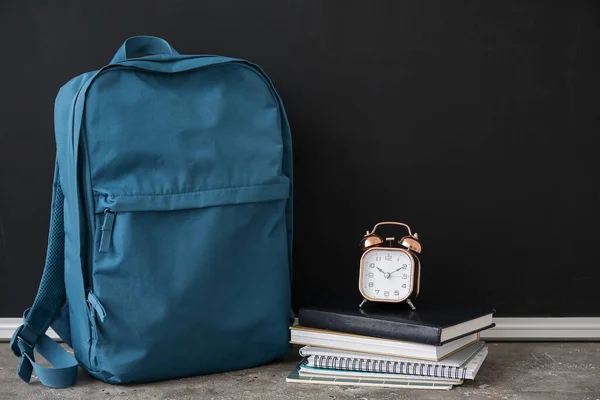 靠近黑色黑板的蓝色校服背包 上面有笔记本和闹钟 — 图库照片