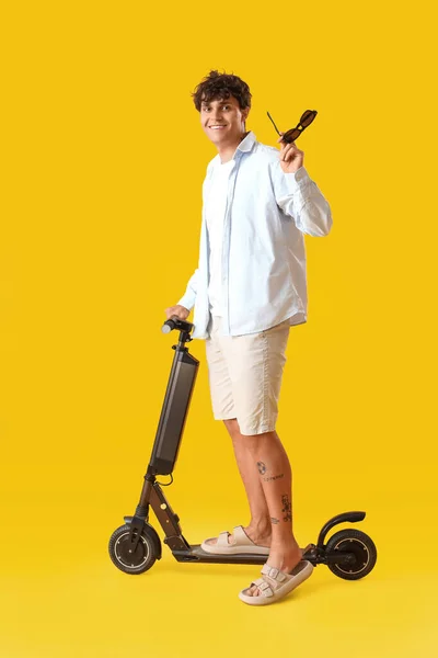 Sarı Arka Planda Güneş Gözlüklü Elektrikli Scooterlı Genç Adam — Stok fotoğraf