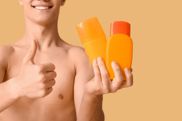 幸せな若いです男とともにボトルの日焼け止めクリームショー親指アップジェスチャーでオレンジの背景 — ストック写真