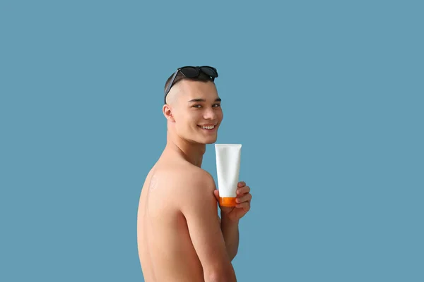 Szczęśliwy Młody Człowiek Okularach Przeciwsłonecznych Butelką Kremu Opalania Niebieskim Tle — Zdjęcie stockowe