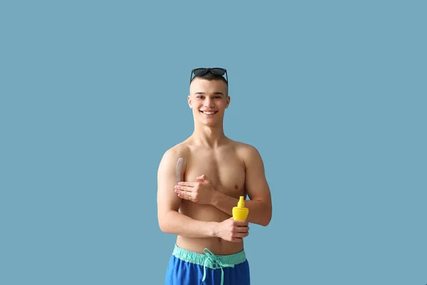 Gelukkig Jongeman Zonnebril Aanbrengen Zonnebrandcrème Zijn Lichaam Tegen Blauwe Achtergrond — Stockfoto