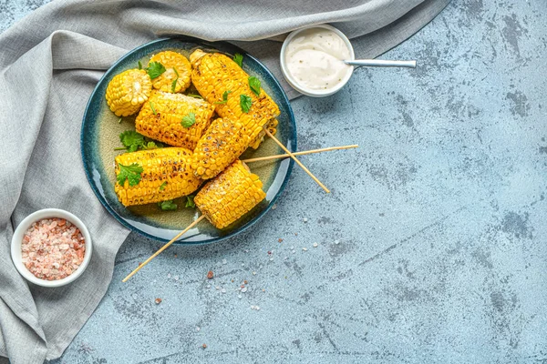 stock image Plate with tasty grilled corn cob skewers and parsley on blue background