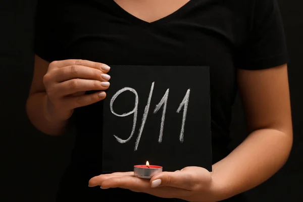 Woman holding board with date of National Day of Prayer and Remembrance for the Victims of the Terrorist Attacks, burning candle on black background