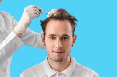 Genç adam mavi arka planda saç büyümesi için serum alıyor, yakın plan.