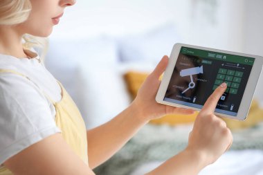 Yatak odasında akıllı ev güvenlik sistemi kontrol paneli kullanan genç bir kadın.