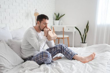 Elinde kese kağıdıyla yatak odasında panik atak geçiren genç bir adam.