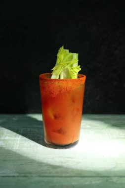 Koyu yeşil arka planda, ahşap masada kerevizli bir bardak Bloody Mary.