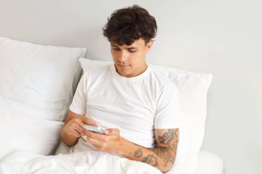 Genç adam yatakta cep telefonu kullanıyor.