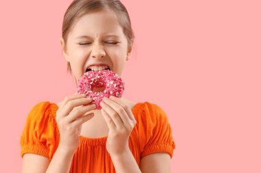 Küçük kız pembe arka planda lezzetli donut yiyor, yakın plan.