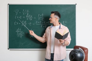 Erkek Matematik öğretmeni sınıfta tahtaya yakın bir yerde ders veriyor.