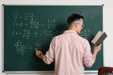 Erkek Matematik öğretmeni sınıfta tahtaya yakın bir yerde ders veriyor.