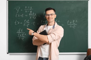 Erkek Matematik öğretmeni sınıfta tahtaya yakın bir yerde ders veriyor.