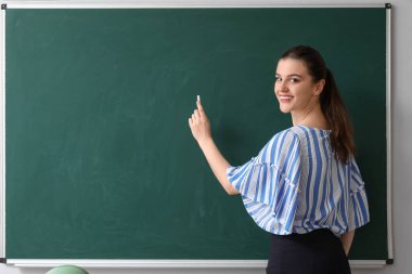 Sınıfta yazı tahtasının yanında bayan öğretmen.