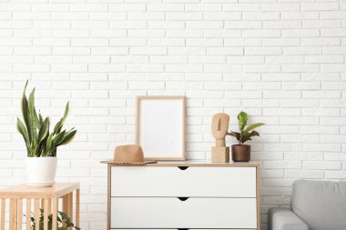 Çekmeceleri, boş çerçevesi ve çiçekleri olan aydınlık oturma odasının içinde.