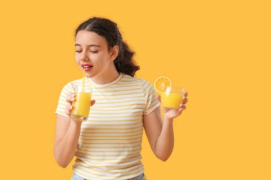 Sarı arka planda portakal suyu bardakları olan genç bir kız.