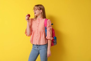 Sarı arka planda elma ve sırt çantalı kız öğrenci.