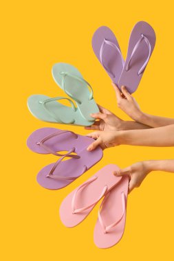 Sarı arka planda farklı parmak arası terlikleri olan eller.