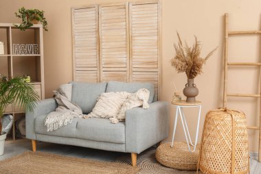 Aydınlık oturma odasının içinde şık gri kanepe, raf ünitesi, katlanır ekran ve merdiven