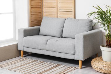 Aydınlık oturma odasının içinde şık gri kanepe, katlanır ekran ve çiçekli