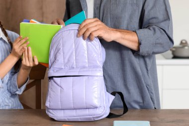 Babası küçük kızına mutfakta okul çantasını toplaması için yardım ediyor.