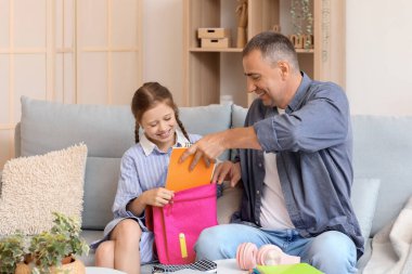 Babası küçük kızına okul çantasını toplaması için yardım ediyor.