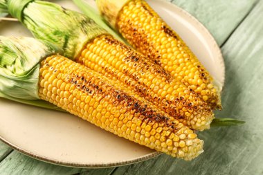 Yeşil ahşap arka planda lezzetli ızgara mısır koçanı tabağı.